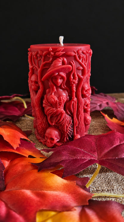 Red Bonekeeper witch candle with a staff, skulls and sculpted branches among autumn leaves.