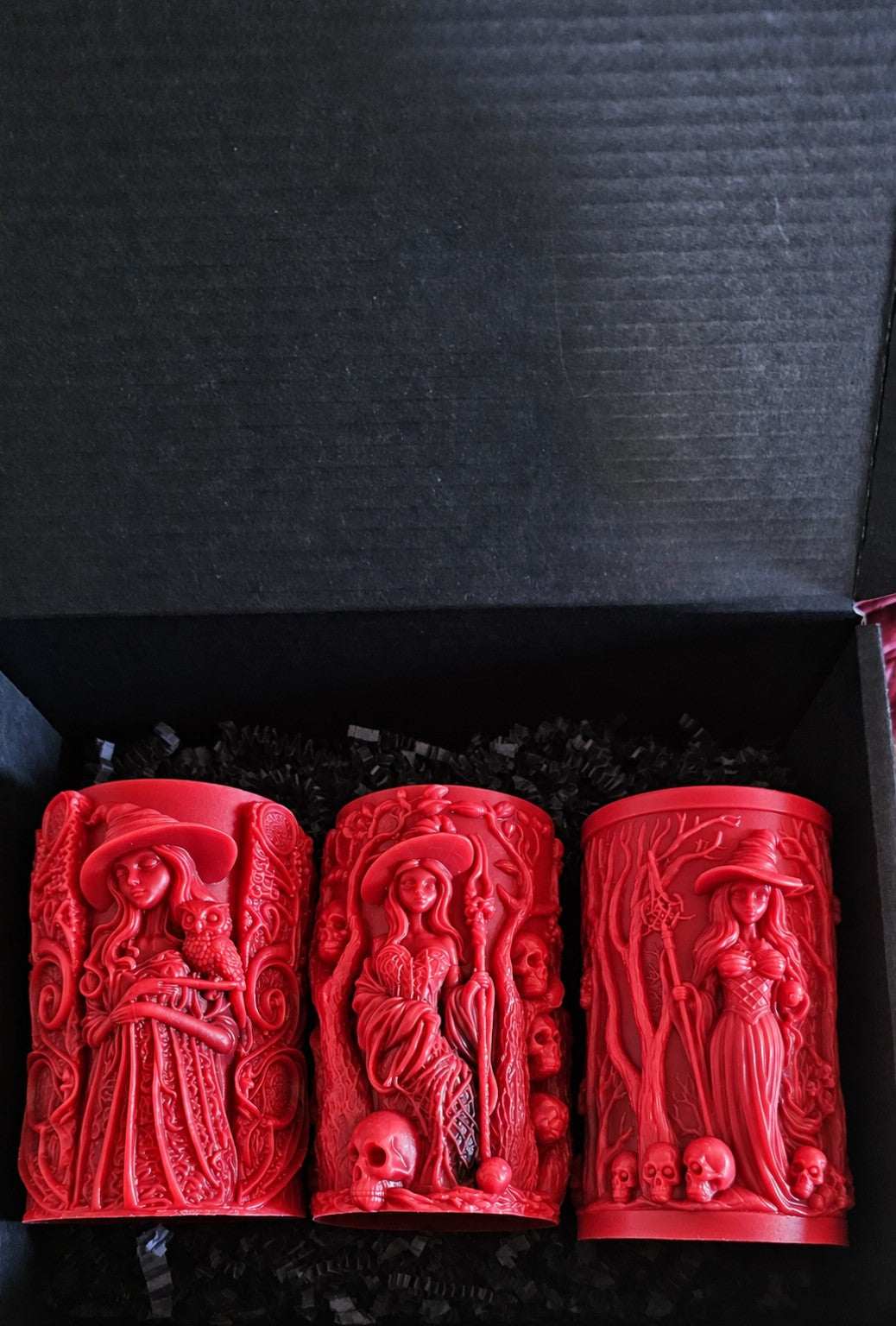 Wisdomkeeper, Bonekeeper and Grovekeeper red candles together in a black box with black paper shred.
