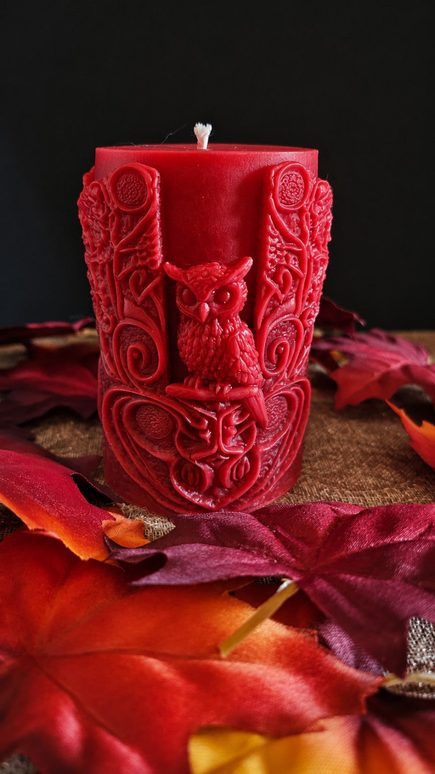 Back of the red Wisdomkeeper candle showing a sculpted owl and winding woodland details.