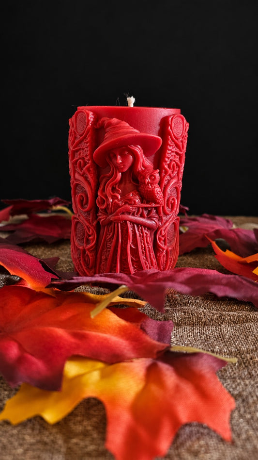 Red Wisdomkeeper sculptural witch candle with an owl, surrounded by autumn leaves.